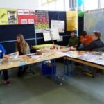 Schüler präsentieren an Tischen verschiedene Materialien und Projekte.
