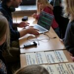 Mann am Laptop zeigt Kindern eine Präsentation mit Textkarten.