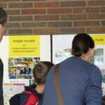 Besucher betrachten Informationen an Plakatwänden in einer Schule.