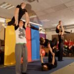 Zwei Gruppen von Akrobaten zeigen verschiedene Pyramidenformationen auf einer Bühne.