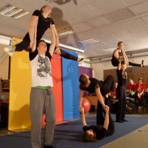 Zwei Gruppen von Akrobaten zeigen verschiedene Pyramidenformationen auf einer Bühne.