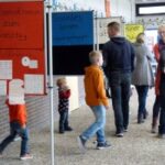 Besucher in einer Schule betrachten Informationsstände in einem Flur.
