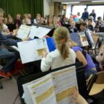 Schülerinnen und Schüler musizieren im Orchester unter Leitung eines Lehrers.