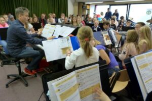 Schülerinnen und Schüler musizieren im Orchester unter Leitung eines Lehrers.