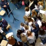 Gruppengesang mit Schülern vor einem Pianisten in einem Schulflur.