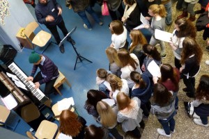 Gruppengesang mit Schülern vor einem Pianisten in einem Schulflur.