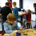 Eine Gruppe Kinder arbeitet an Holzprojekten in einem Werkraum.