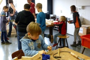 Eine Gruppe Kinder arbeitet an Holzprojekten in einem Werkraum.