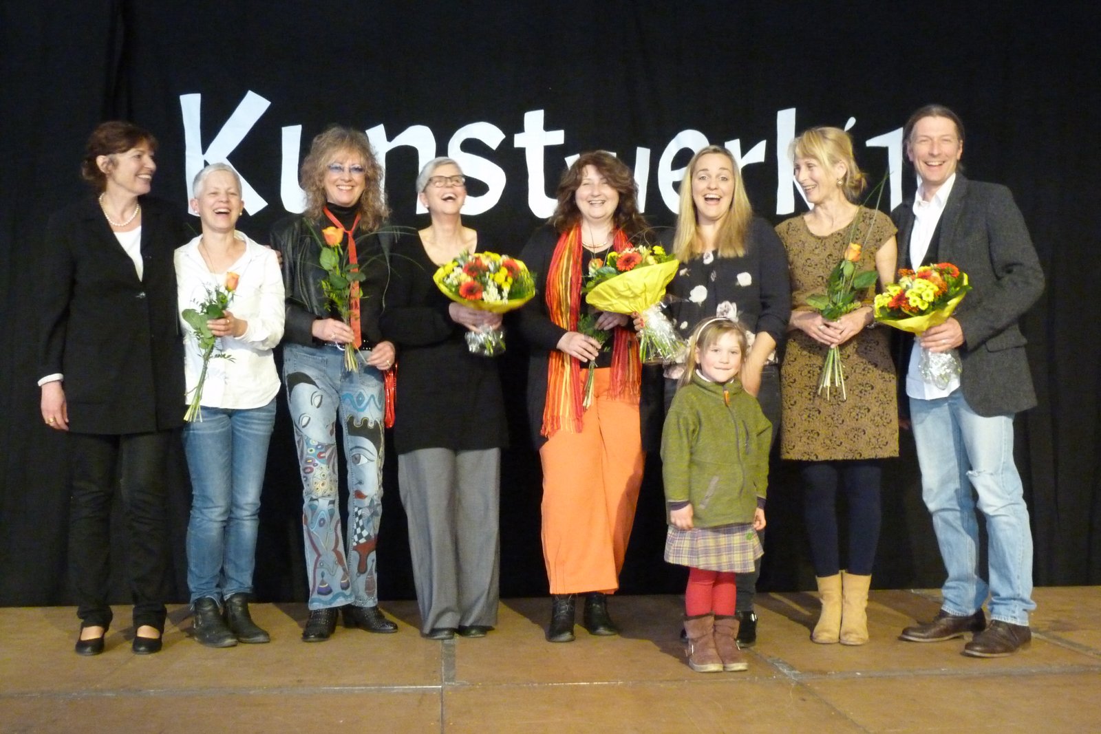 Gruppenfoto von Frauen und einem Mädchen auf einer Bühne, Blumen in der Hand.