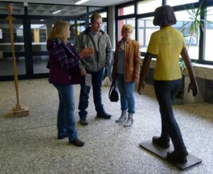 Vier Personen unterhalten sich in einer Schule, neben ihnen steht eine Statue.