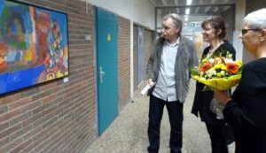 Besucher betrachten ein Kunstwerk in einer Schule, Blumenstrauß in der Hand.