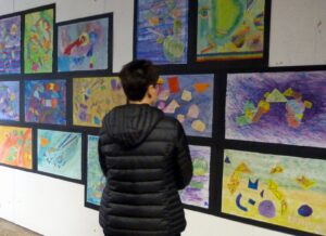 Besucher betrachtet eine Ausstellung mit bunten Zeichnungen an der Wand.