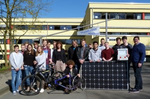Schülergruppe mit Solarzelle und Fahrrad vor der Schule.