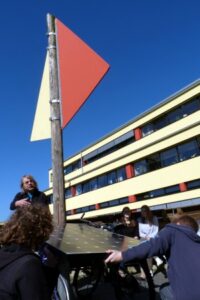 Menschen heben ein Kunstwerk mit einem roten und orangefarbenen Dreieck.