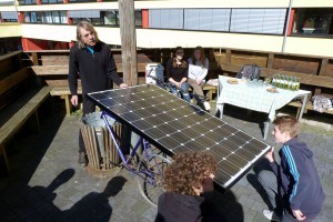 Schüler präsentieren ein Fahrrad mit Solarpanel in einem Schulhof.