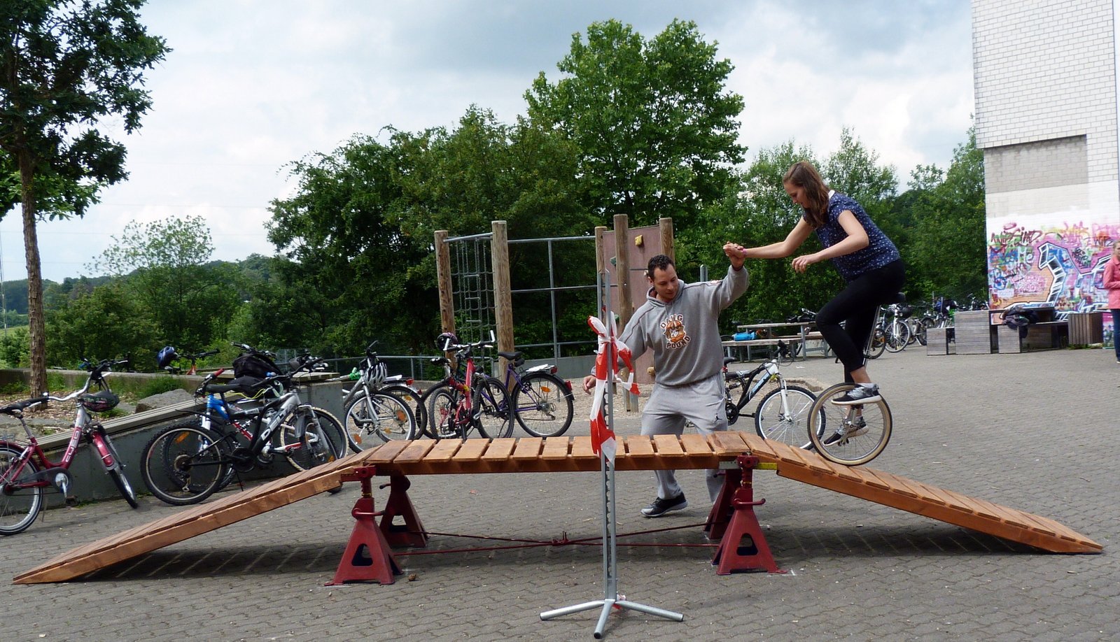 Zwei Personen auf einer Holzrampe, Fahrräder im Hintergrund.