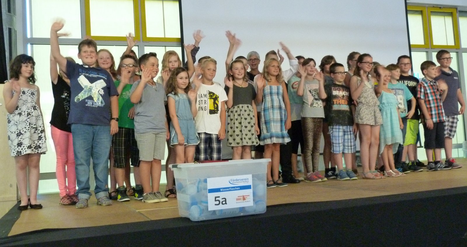 Schüler der Klasse 5a stehen auf der Bühne und winken in die Kamera.