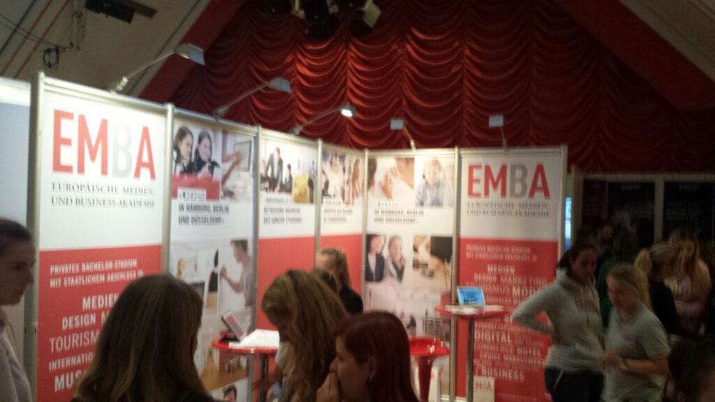 Messestand mit EMBA-Displays, viele Besucher stehen davor.