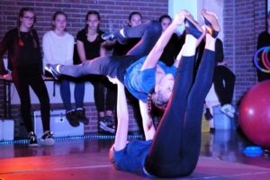 Zwei Sportlerinnen führen eine Partnerakrobatik-Übung auf einer Bühne vor.
