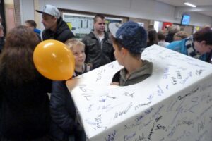 Schüler mit Luftballon und Kasten, der mit Unterschriften bemalt ist.