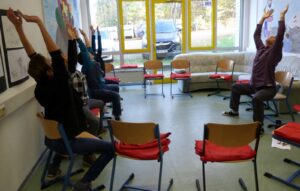 Gruppensitzung mit Teilnehmern, die in einem Raum Streckübungen machen.