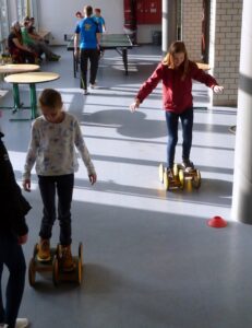 Zwei Kinder fahren auf Hoverboards in einem lichtdurchfluteten Raum.