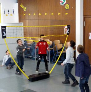 Kinder spielen Volleyball in der Schule an einem Aufstellnetz.