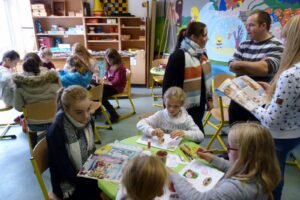 Kinder und Erwachsene arbeiten an Tischen in einem bunten Raum.