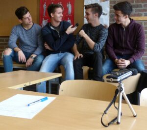 Vier Jugendliche sitzen an Tischen und unterhalten sich. Ein Mikrofon ist sichtbar.