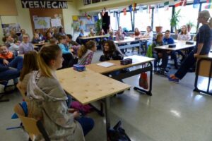 Schüler in einem Klassenraum sitzen an Tischen und hören einem Lehrer zu.