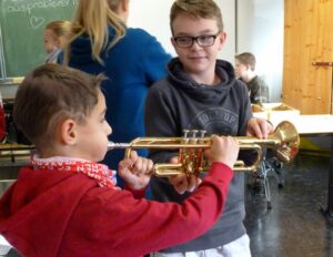 Zwei Kinder halten eine Trompete in einem Klassenraum.