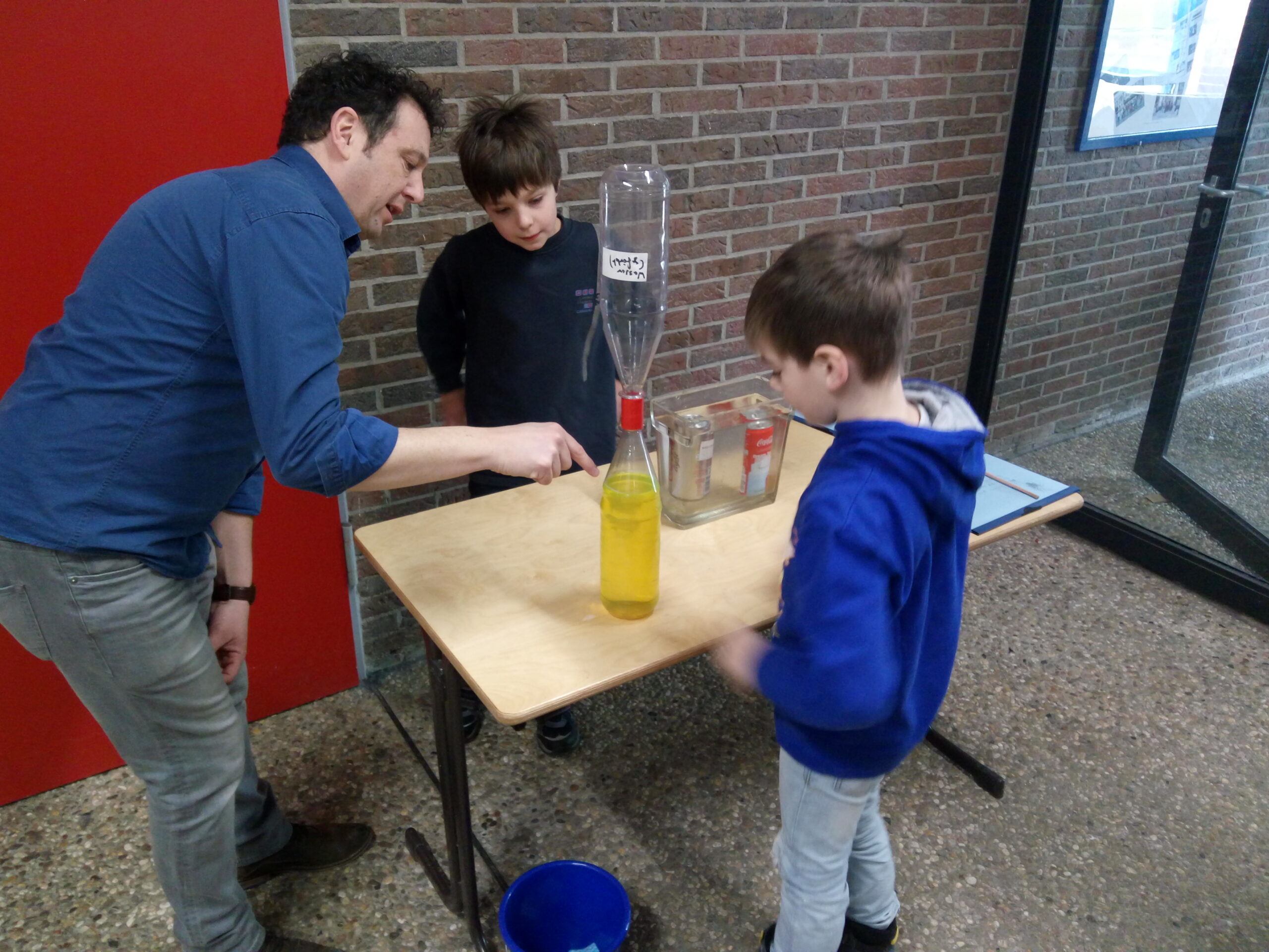 Lehrer zeigt zwei Kindern ein Experiment mit Flüssigkeiten.