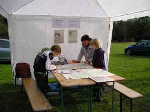 Drei Personen stehen an einem Tisch in einem Zelt und betrachten Karten.