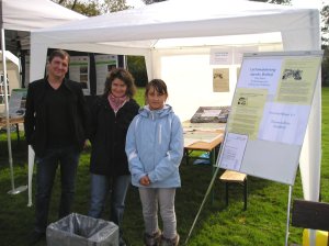 Drei Personen stehen an einem Informationsstand im Freien.