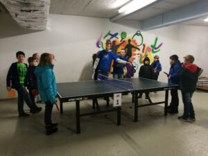 Tischtennistraining mit Kindern in einem Raum, Tischtennisplatte im Vordergrund.