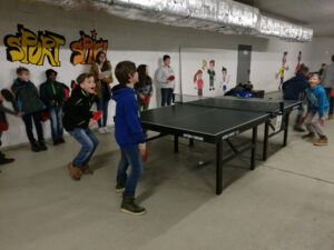 Kinder spielen Tischtennis in einer Sporthalle.