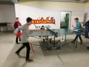 Kinder spielen Tischtennis in einem Raum mit einer bunten Wandgestaltung.