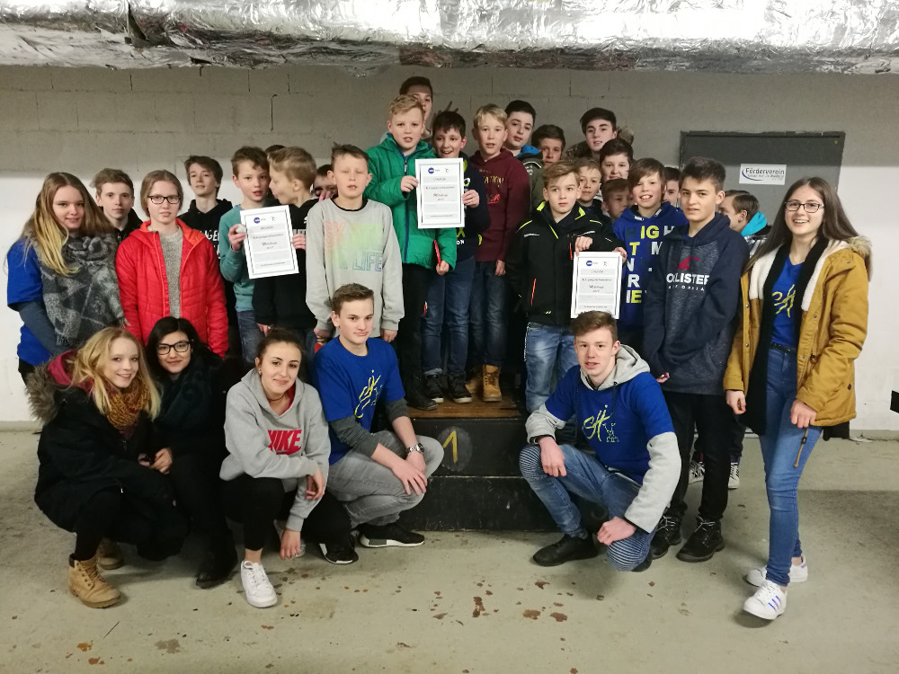 Gruppe von Jugendlichen, die stolz Urkunden halten, stehen auf einer Bühne.