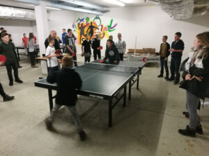 Gruppenspiel mit Jugendlichen am Tischtennistisch in einem Keller.