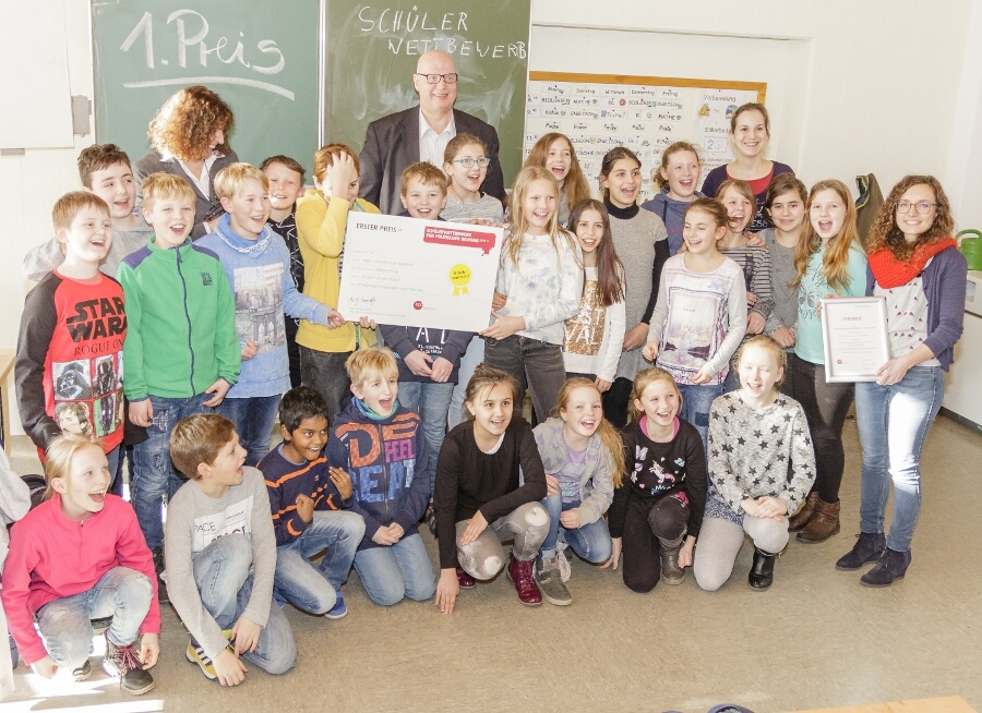 Schülergruppe mit Lehrern in einem Klassenraum, sie halten Urkunden und Plakate.
