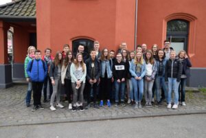 Gruppenfoto von Schülern und Lehrern vor einem roten Gebäude.