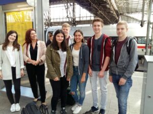 Gruppe von Schülerinnen und Schülern am Bahngleise. Zug im Hintergrund.