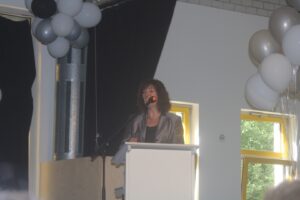 Frau spricht am Rednerpult, im Hintergrund sind Luftballons zu sehen.