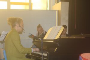 Ein Musiker spielt Klavier, im Hintergrund zwei weitere Musiker.