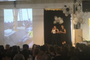 Zwei Frauen präsentieren auf einer Bühne, im Hintergrund eine Projektionsleinwand.