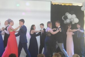 Tanzende Schülerinnen und Schüler in festlicher Kleidung auf einer Bühne.