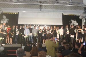 Abschlussfeier mit Schülern auf der Bühne, Urkundenüberreichung und Dekoration.