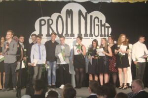 Schüler stehen auf der Bühne bei einer Abschlussfeier mit Urkunden und Blumen.