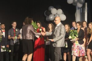 Überreichung von Diplomen bei einer Feier, der Saal ist mit Ballons dekoriert.