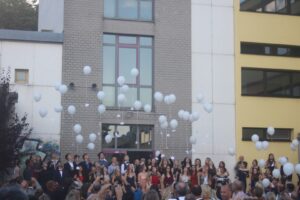 Gruppierung von Personen, die weiße Luftballons in den Himmel steigen lassen.
